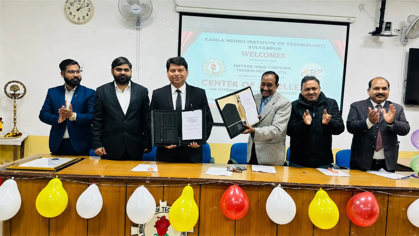 SSS India and KNIT representatives exchanging signed folders on stage, under a screen welcoming SSS India